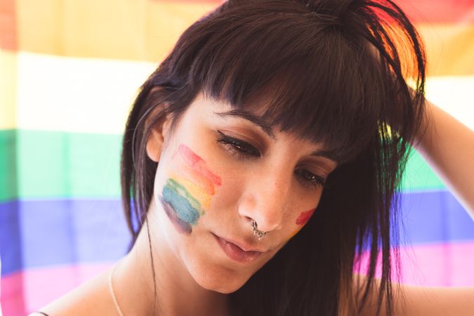 Brunette woman with LGBTQIA symbol on face straightening hair