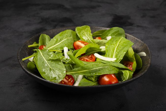 Arugula salad with tomatoes on dark background.