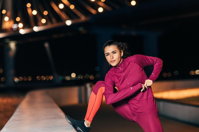 Woman in dark red sportswear stretching her legs in the evening