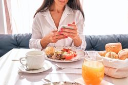 Crop female at table with served breakfast and browsing smartpho