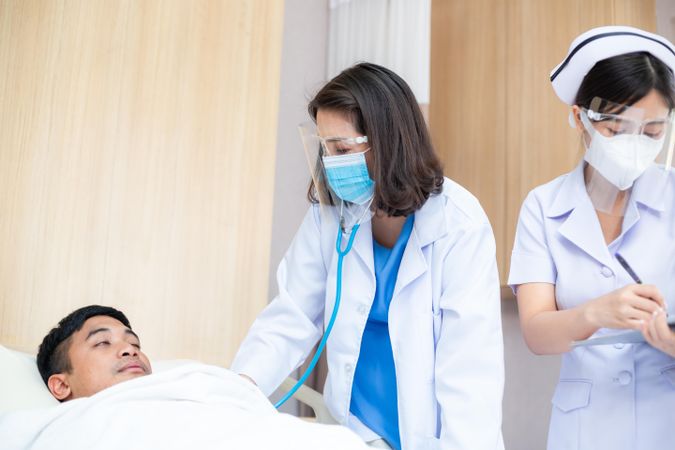 Female doctor checking on sleeping male patient with nurse updating chart
