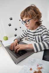 Boy in eyeglasses typing on laptop at home