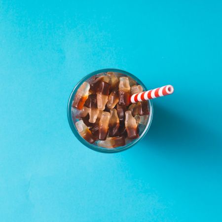 Glass full of gummy candies with straw on blue background