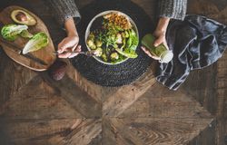 Healthy vegetarian bowl pictured on table with smoothie on side and hands with fork, copy space