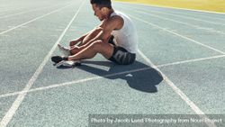 Athlete sitting on a running track tying shoe lace 5p2xeb