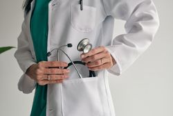 Crop physician in medical robe with stethoscope