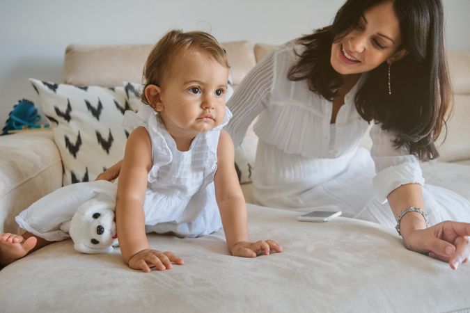 Mother playing with little girl on sofa at home