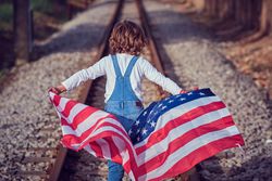 Kid holding USA flag while walking on rails