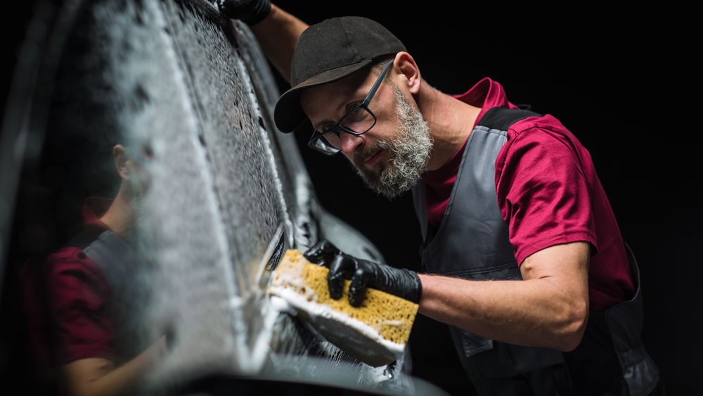 Professional Car Wash Specialist Spreading Foam with a Soft Sponge to Prepare a Modern  Electric SUV with Contemporary Design at a Dealership Car Center.