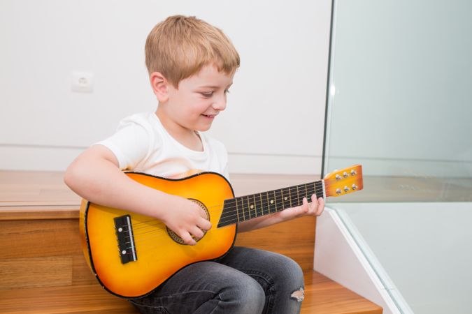 Young blonde boy playing toy guitar