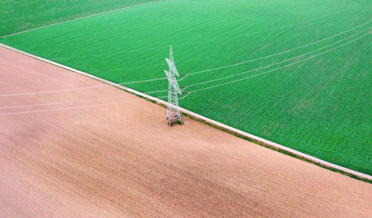 Aerial view with electricity pylon in the middle of agricultural fields