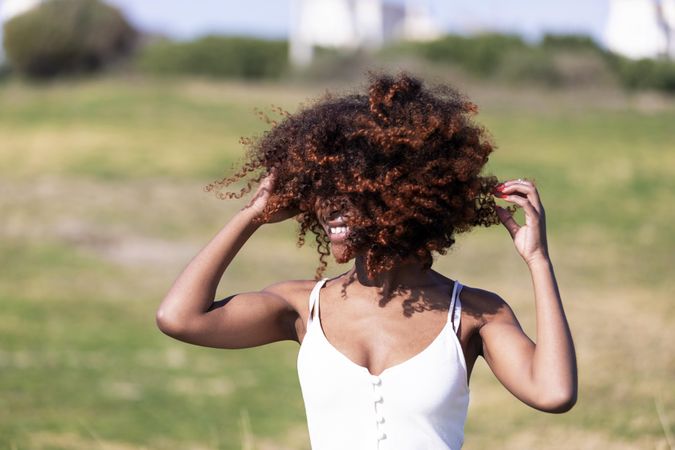 Female pictured outside in park playing with her curly hair in the wind