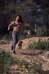 Active young Hispanic sportswoman with dog running along rough p