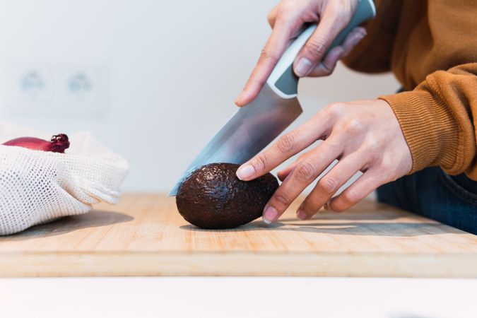 Crop woman cutting avocado in kitchen