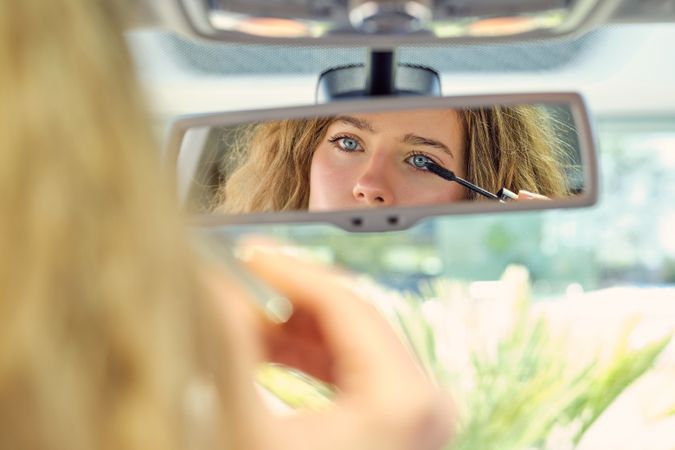 Attractive woman applying mascara and looking in rearview mirror