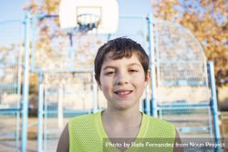 Portrait of a young teen male with sleeveless standing on a street basket court while smiling at camera 0Kdp75