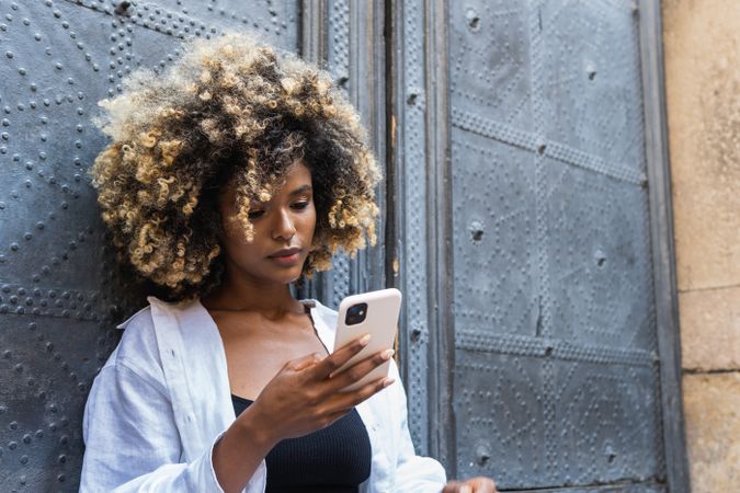 Young Black woman speaking on smartphone while sitting near building