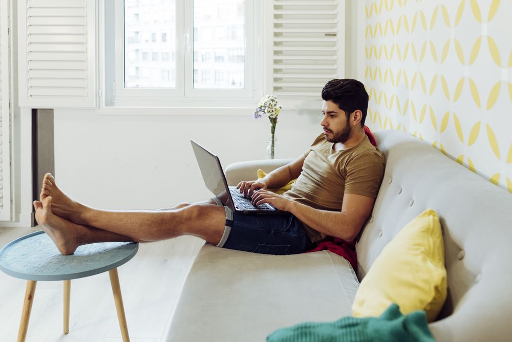 Young pensive male with laptop sitting on sofa