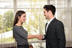 Male and female business colleagues smiling and shaking hands in front of window