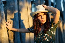 Female brunette leaning against wooden fence outside at sunset