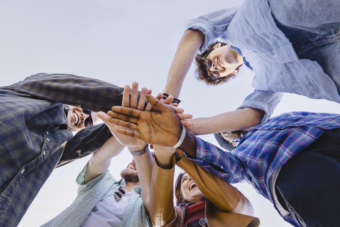 Diverse group of young people joining hands in circle from low angle