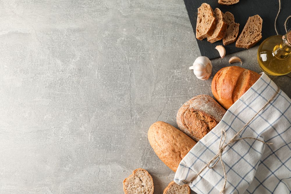 Composition with bakery products, garlic, olive oil and kitchen towel on grey background, top view and space for text