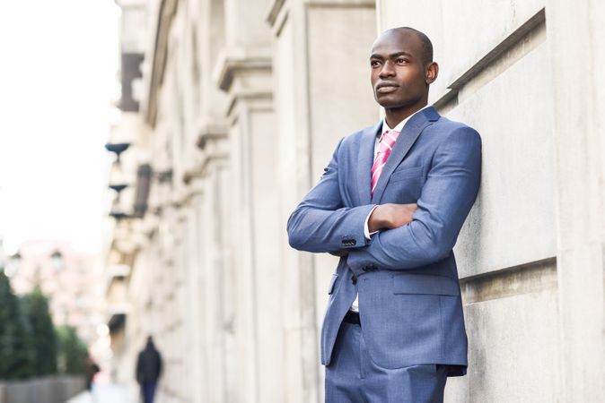 Serious male in business attire leaning on wall with arms closed, copy space