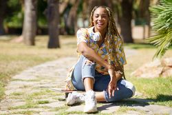 Smiling female sitting on skateboard walkway in park