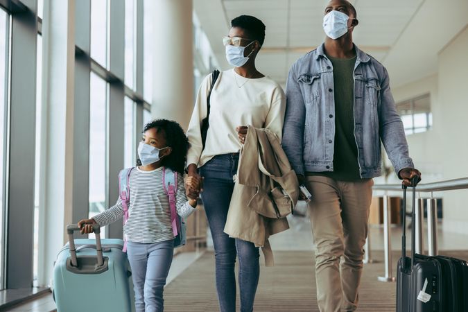 Family in face masks at airport terminal going for holiday looking away