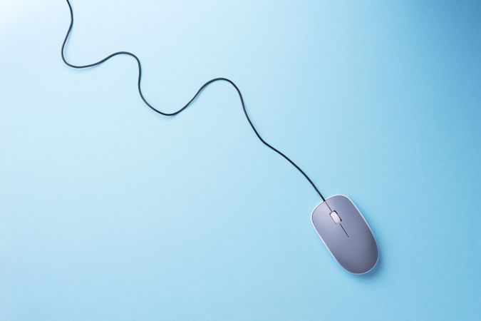 Computer mouse with cable attached laying diagonally on light blue background in