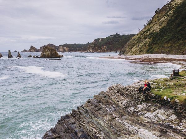 Woman and man sitting on stony green seashore