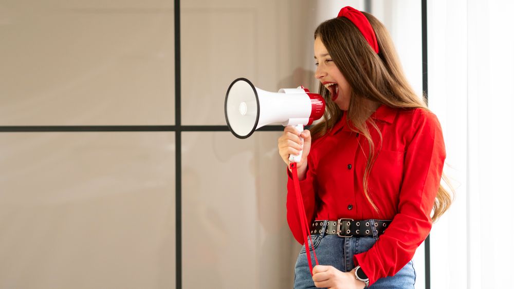Teen girl smiling and speaking loudly into white megaphone.