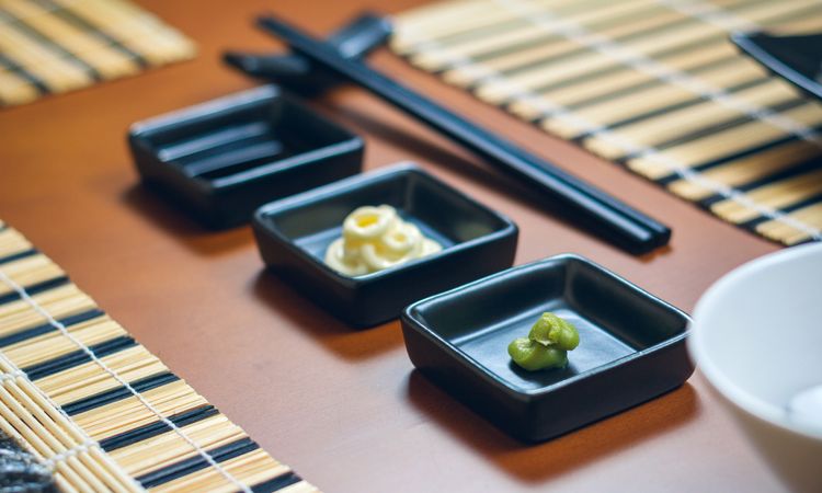 Closeup of saucers with wasabi, mayonnaise and soy sauce ready to eat sushi