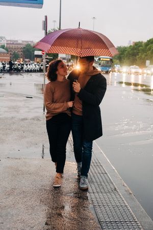Happy couple with umbrella hugging on wet street