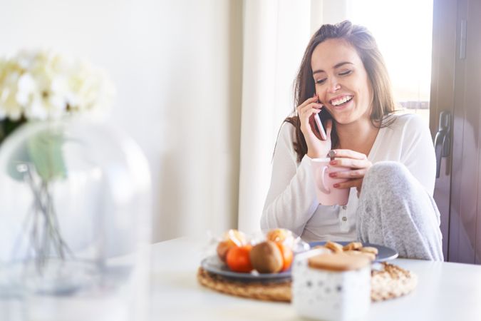Smiling woman with smartphone eating at table at home