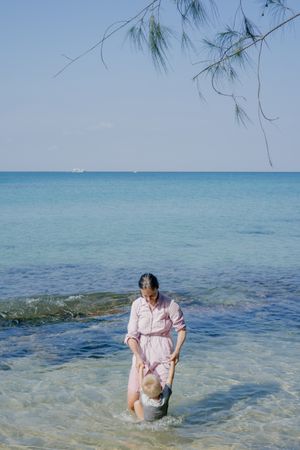 Woman and small kid having fun with water while relaxing on seacoast at resort