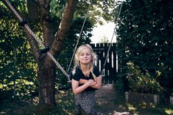 Happy blonde girl with braided hair sitting on outdoor swing