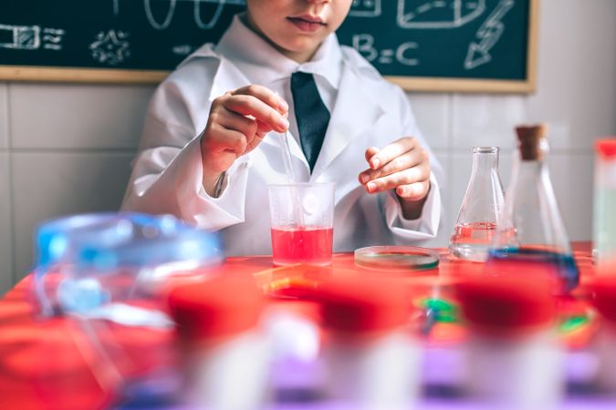 Kid playing in lab coat at with colorful liquids