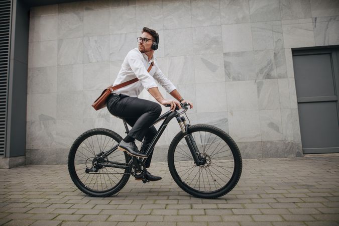 Man wearing office bag and wireless earphones riding a bicycle