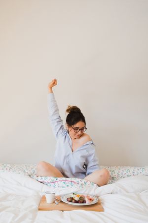 Young woman with breakfast on bed stretching out