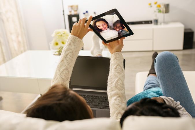 Two women kicking back on a sofa taking selfie on a digital tablet