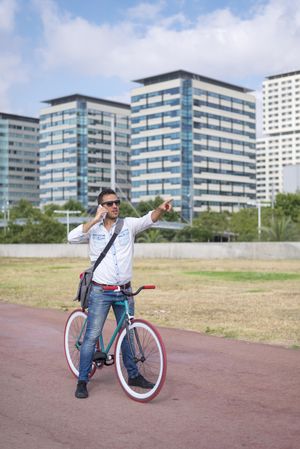 Male with colorful bicycle having conversation on phone and pointing in distance on city bike path