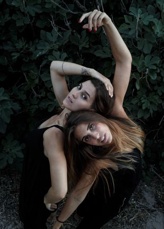 Young women posing near green bush
