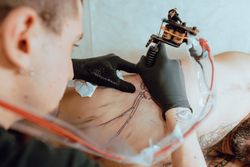 Tattoo artist working on client' chest