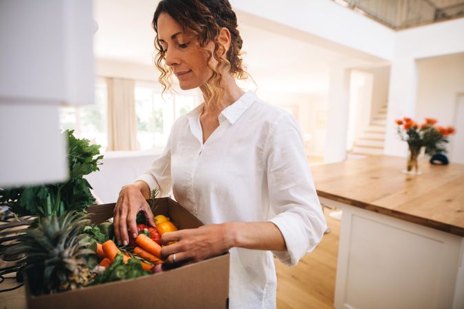 Woman in her kitchen with a box full of organic vegetable