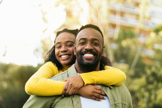 smiling Black man giving piggyback ride to his girlfriend, front view