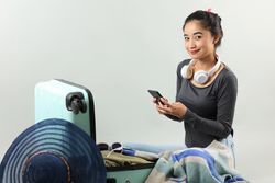 Traveler Asian Young Woman Check List on Her Phone after Packing