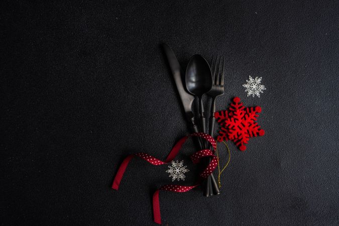 Dark cutlery on dark background tied with festive red ribbon and snow flake ornament