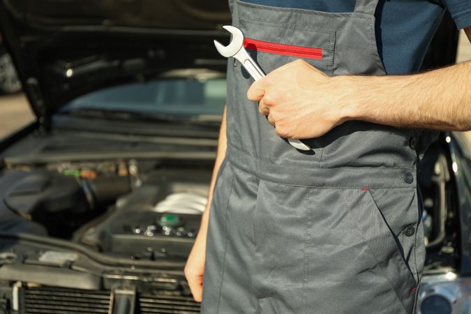 Man in overalls holding a wrench. Car inspection