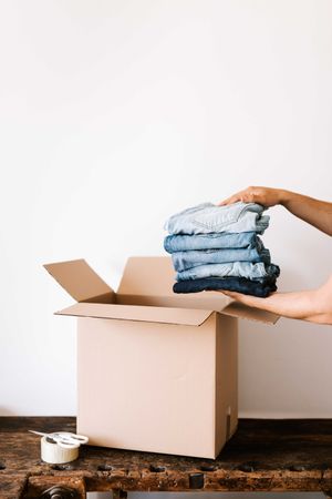 Cropped image of person holding stack of folded t-shirt beside cardboard box